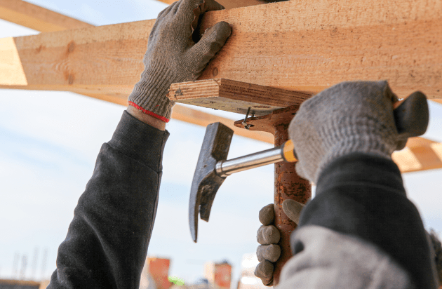 A closeup of a person hammering a nail into a wooden frame.