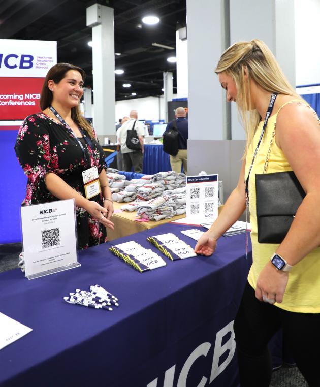 NICB membership director speaking to a woman in a yellow shirt at a booth.